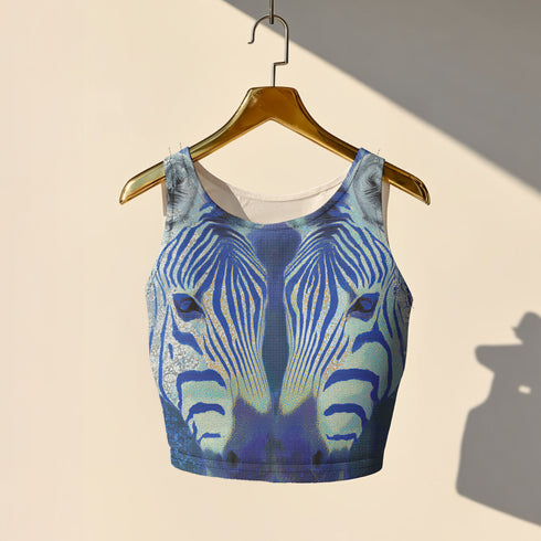 A women's sleeveless, high-neck crop top made from a performance spandex knit fabric. The top is designed with a body-hugging fit and features a striking, symmetrical digital graphic of a zebra's face. The intricate print uses shades of electric blue, cobalt, and navy, contrasted with a shimmering silver glitter effect that outlines the zebra's stripes and features. The psychedelic, futuristic design covers the entire front of the shirt.